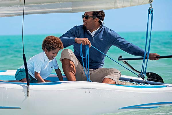 A lifestyle image from Vineyard Vines showing a dad and his son sailing